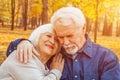 Happy elderly man and woman sitting on a bench in autumn day. Relaxed senior couple sitting on a park bench. Grandfather gently Royalty Free Stock Photo