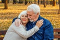 Happy elderly man and woman sitting on a bench in autumn day. Relaxed senior couple sitting on a park bench. Grandfather gently Royalty Free Stock Photo