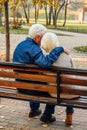 Happy elderly man and woman sitting on a bench in autumn day. Relaxed senior couple sitting on a park bench. Grandfather gently Royalty Free Stock Photo