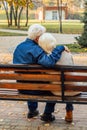 Happy elderly man and woman sitting on a bench in autumn day. Relaxed senior couple sitting on a park bench. Grandfather gently Royalty Free Stock Photo