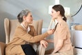 Happy elderly middle mother sitting on chair touching a strand of daughter`s hair, looking each other