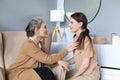 Happy elderly middle mother sitting on chair touching a strand of daughter`s hair, looking each other