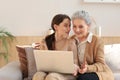 Happy elderly middle mother sitting on couch with her daughter, looking at laptop. Young woman showing video Royalty Free Stock Photo