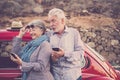 Happy elderly senior couple use mobile phones outdoor near a red beautiful retro car. leisure activity and travel together forever Royalty Free Stock Photo