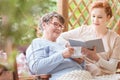 Happy elderly woman drinking tea and nurse reading her a book in Royalty Free Stock Photo