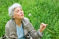 Happy elderly woman sitting on a meadow blowing on a dandelion Royalty Free Stock Photo