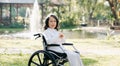 Happy elderly woman sitting on wheelchair outdoor in park relax your mind with green nature. Nursing home hospital garden concept