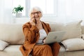 a happy elderly woman smiles sweetly sitting on the sofa in a bright apartment near the window and talking on a Royalty Free Stock Photo