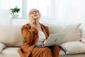 a happy elderly woman smiles sweetly sitting on the sofa in a bright apartment near the window and talking on a Royalty Free Stock Photo