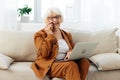 a happy elderly woman smiles sweetly sitting on the sofa in a bright apartment near the window and talking on a Royalty Free Stock Photo