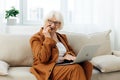 a happy elderly woman smiles sweetly sitting on the sofa in a bright apartment near the window and talking on a Royalty Free Stock Photo