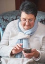 Happy elderly woman using smartphone texting browsing on mobile phone sending messages sitting on couch at home Royalty Free Stock Photo