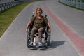 Happy elderly woman on a wheelchair rides along a bike path.