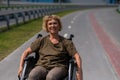 Happy elderly woman on a wheelchair rides along a bike path.