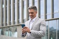 Happy elegant middle aged business man in suit using phone standing outdoor. Royalty Free Stock Photo