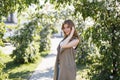 Happy elegant young woman in fashionable summer clothes posing in a park near a green flowering trees. Beautiful girl with a Royalty Free Stock Photo