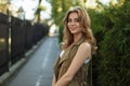 Happy elegant young woman in trendy summer dress with stylish black leather handbag posing on the street near green trees and an Royalty Free Stock Photo