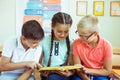 Happy elementary school students sitting on desk and reading a book at school