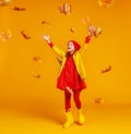 Happy emotional cheerful child girl jumping and laughing with autumn leaves on colored yellow background