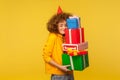 Happy emotions from big mountain of gifts. Portrait of pleased happy curly-haired woman with party cone