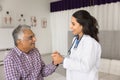 Happy empathetic young doctor touching hand of elderly Indian patient