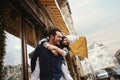 Happy enamored couple is standing outdoors near the decorated shop windows, hugging and kissing each other