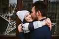 Happy enamored couple is standing outdoors near the decorated shop windows, hugging and kissing each other