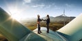 Happy engineer and businessman shake hands after good work. They standing a top of windmill. Around wind generators