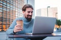 Happy entrepreneur man smiling and working online with a laptop computer, taking a coffee outdoors in a city terrace Royalty Free Stock Photo