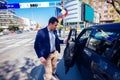 Happy entrepreneur opening his car door and inspecting the interior of his car while being parked next to a busy city boulevard