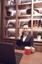 Young woman sitting in coffee shop at wooden table, drinking coffee and using smartphone.On table is laptop Royalty Free Stock Photo