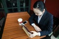 Young woman sitting in coffee shop at wooden table, drinking coffee and using pad.On table is laptop Royalty Free Stock Photo