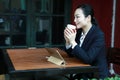 Young woman sitting in coffee shop at wooden table, drinking coffee and using pad.On table is laptop Royalty Free Stock Photo