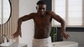 Happy ethnic African American man with bath towel on hips dancing shirtless at bathroom hotel funny naked handsome