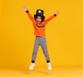 Happy ethnic boy in pumpkin costume jumping and celebrates Halloween on yellow background