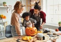 Happy african american family mother, father and child son carving pumpkin for Halloween holiday together at home