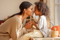 Happy ethnic family mother and son kiss and laugh in the kitchen at home