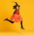 Happy ethnic girl in witch pumpkin costume jumping and celebrates Halloween on yellow background