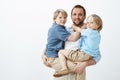 Happy european father holding two boys on hands and smiling broadly, being pleased and loving his sons, united and close