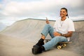 Happy european man using mobile phone while sitting on skateboard on sports ramp, guy smiling at camera, free space Royalty Free Stock Photo