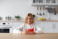 Happy european pretty adolescent blonde girl in casual sits at table with glass of water in minimalist kitchen Royalty Free Stock Photo