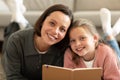 Happy european teenager girl and millennial mom reading book on floor in living room interior, close up Royalty Free Stock Photo