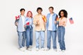 Happy exchange students in language school. Smiling multiracial friends holding different flags over white background Royalty Free Stock Photo