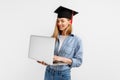Happy excited beautiful graduate girl in a graduation cap on her head using a laptop while standing on a white background. Royalty Free Stock Photo
