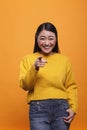 Happy excited beautiful woman wearing yellow sweater pointing index finger at camera on orange background. Royalty Free Stock Photo