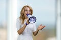 Happy excited blonde middle aged business woman in white dress gives a speech in megaphone. Royalty Free Stock Photo