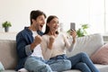 Happy excited caucasian young husband and wife rejoice online victory and look at smartphone together Royalty Free Stock Photo