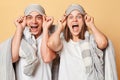 Happy excited couple man and woman wrapped in blanket isolated over beige background raised up blindfolds looking at camera with