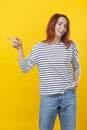 Happy excited cuacaisan winsome ginger girl in striped shirt pointing finger on copy space isolated on golden yellow background