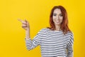 Happy excited cuacaisan winsome ginger girl in striped shirt pointing finger on copy space isolated on golden yellow background